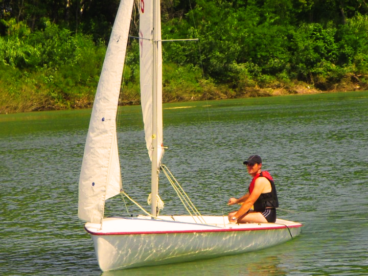 Un homme avec une casquette assis sur le bord de son dériveur qui vogue sur le Rhône.